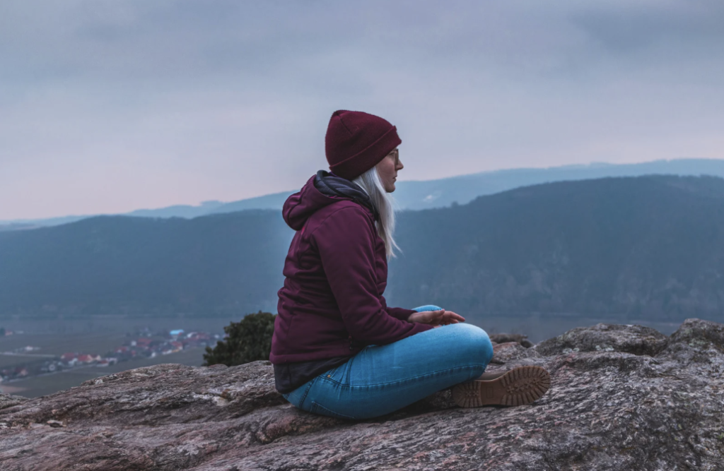 Woman in warm clothes sitting on a rock in the wilderness.
