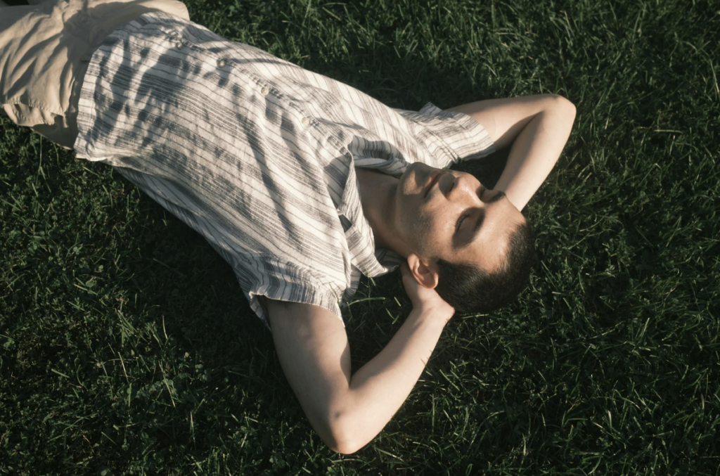 Young man laying in the grass with his eyes closed and arms crossed behind his head.