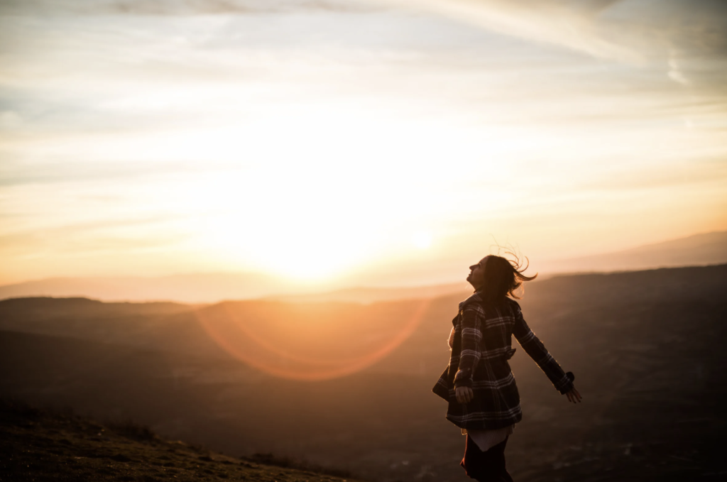 Woman looking at the sunset with open arms. 