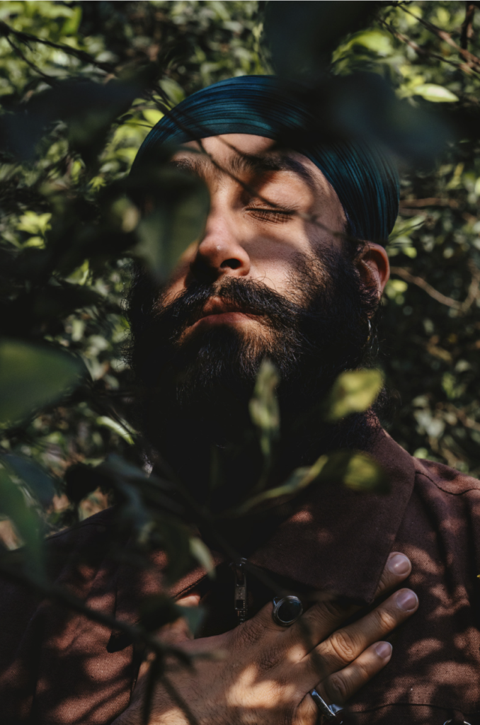 A man standing with his eyes closed in dappled sunlight. 