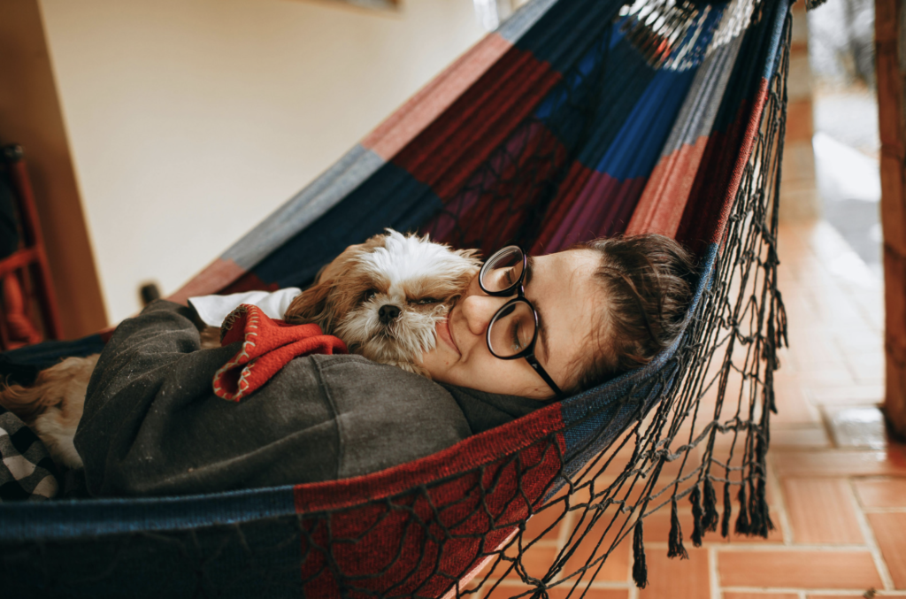 Person laying in a hammock with a dog
