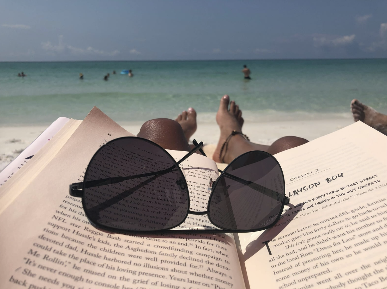 POV laying on a beach with a book and sunglasses in lap